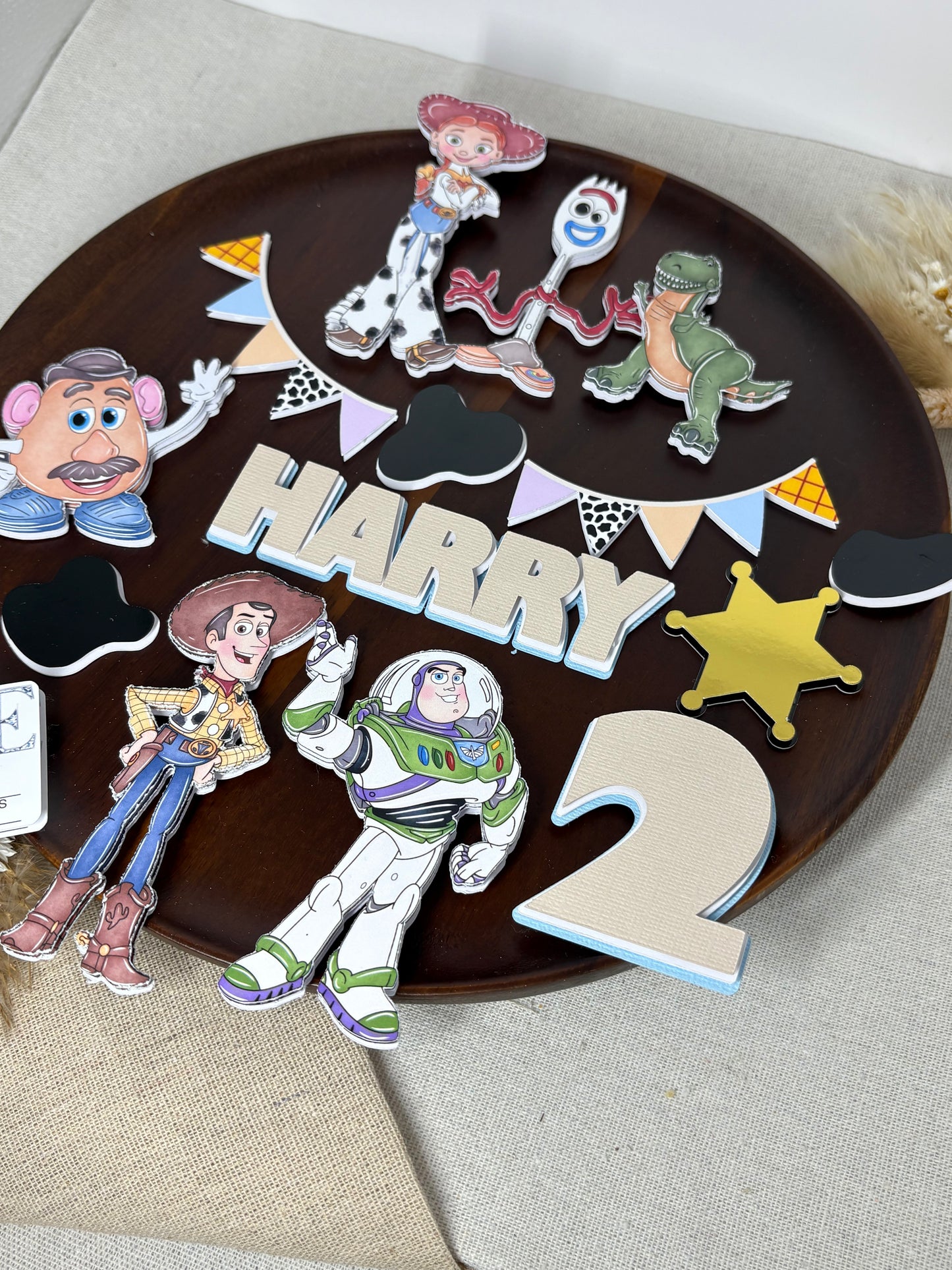 Personalised Toy Story–inspired cake topper set with layered characters, custom name and age, “To Infinity and Beyond” sign, bunting, badge, and cow print charms on a birthday cake.