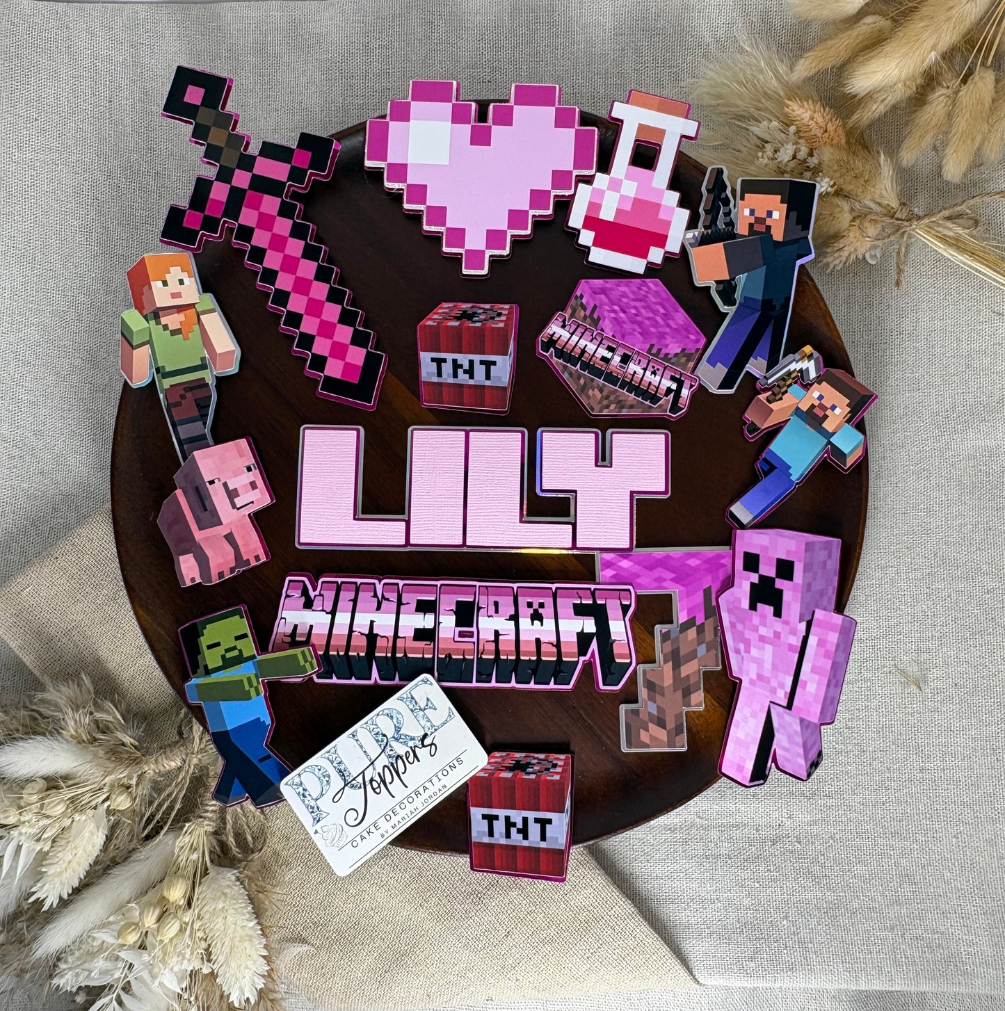 A circular wooden sign featuring Minecraft-themed cutouts and the text 'LIFELONG JROPTER' in pink and white, styled on a beige fabric background with dried wheat sprigs.