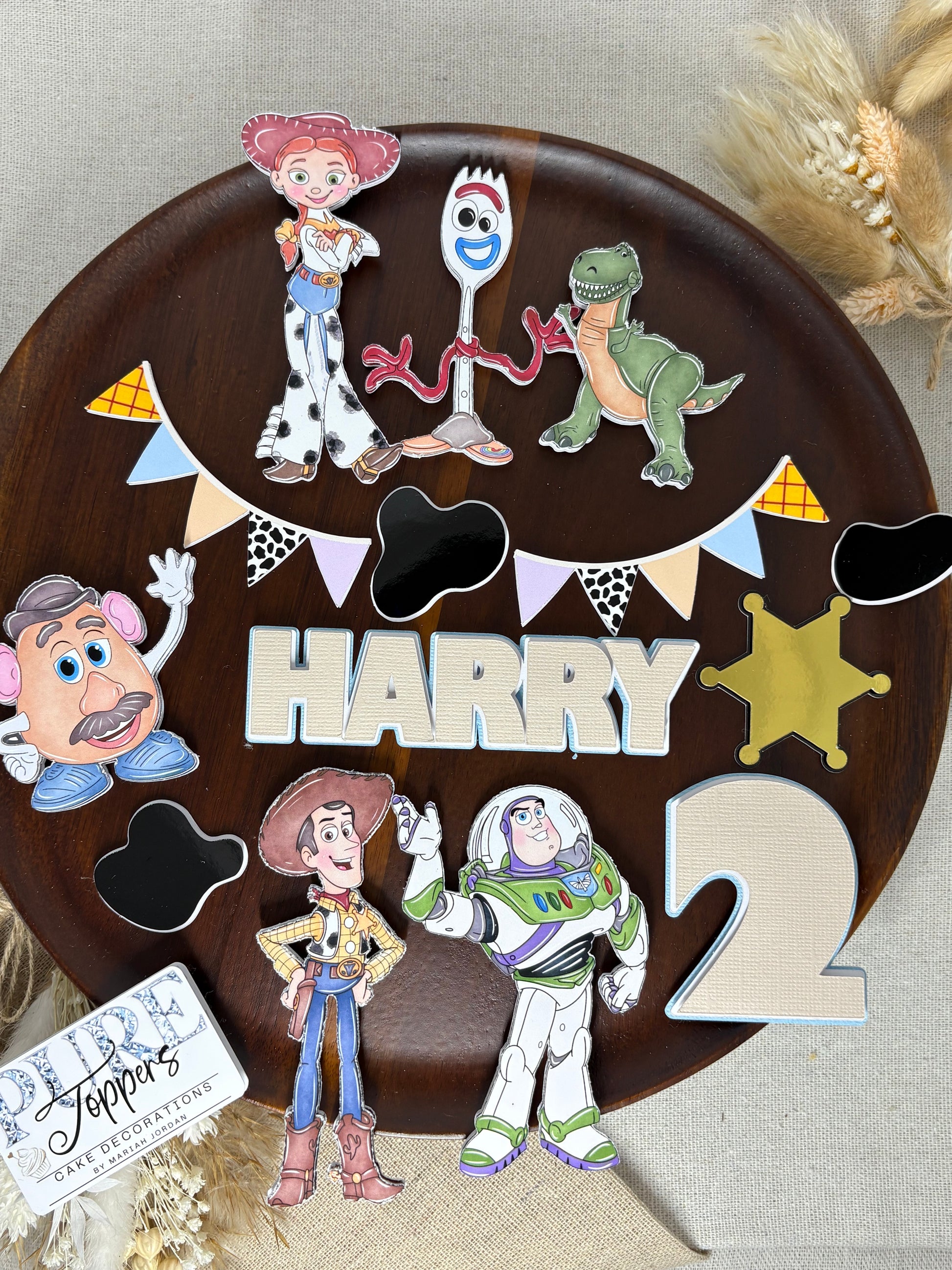 Personalised Toy Story–inspired cake topper set with layered characters, custom name and age, “To Infinity and Beyond” sign, bunting, badge, and cow print charms on a birthday cake.