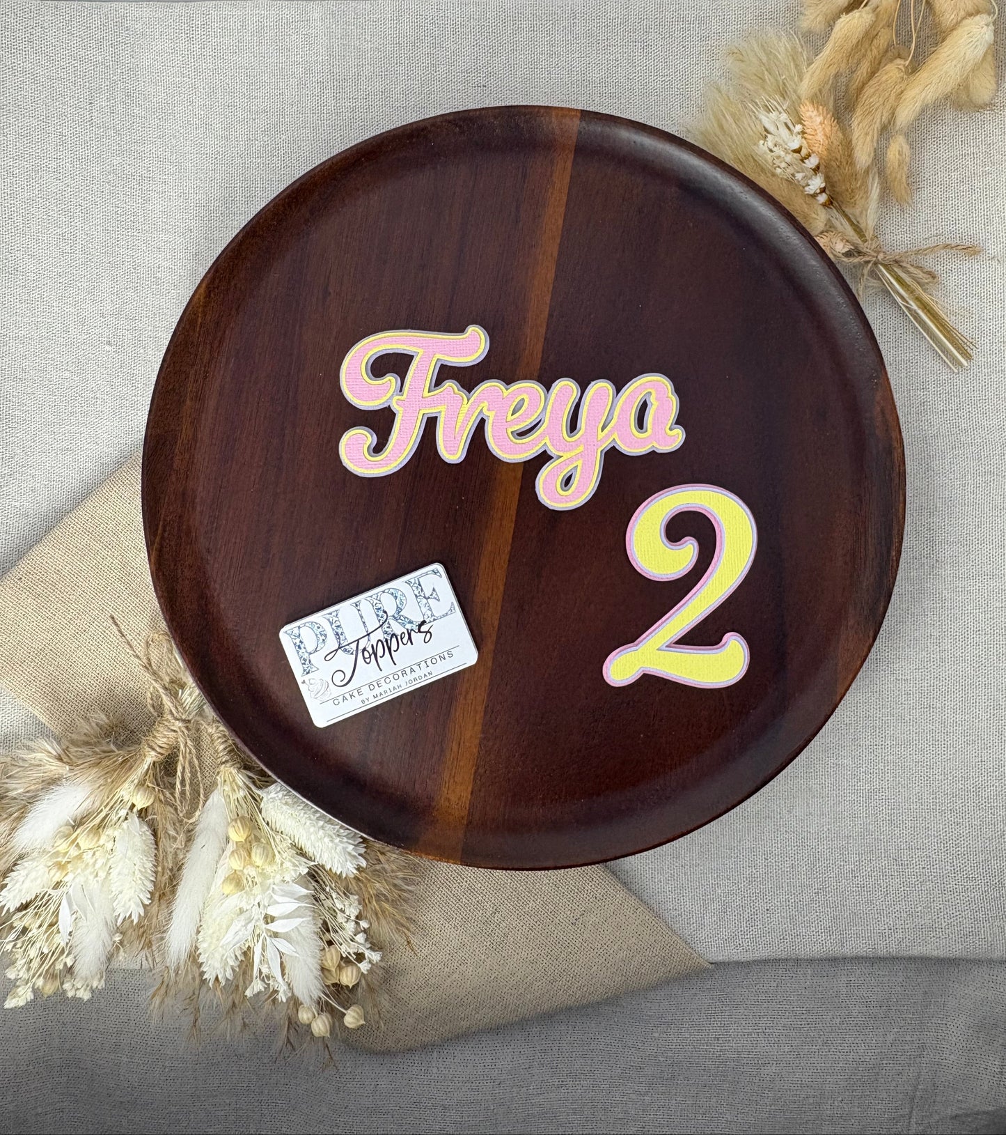Pastel triple-layered personalised name and age cake topper in pink, yellow, and purple displayed for birthday cake decoration.