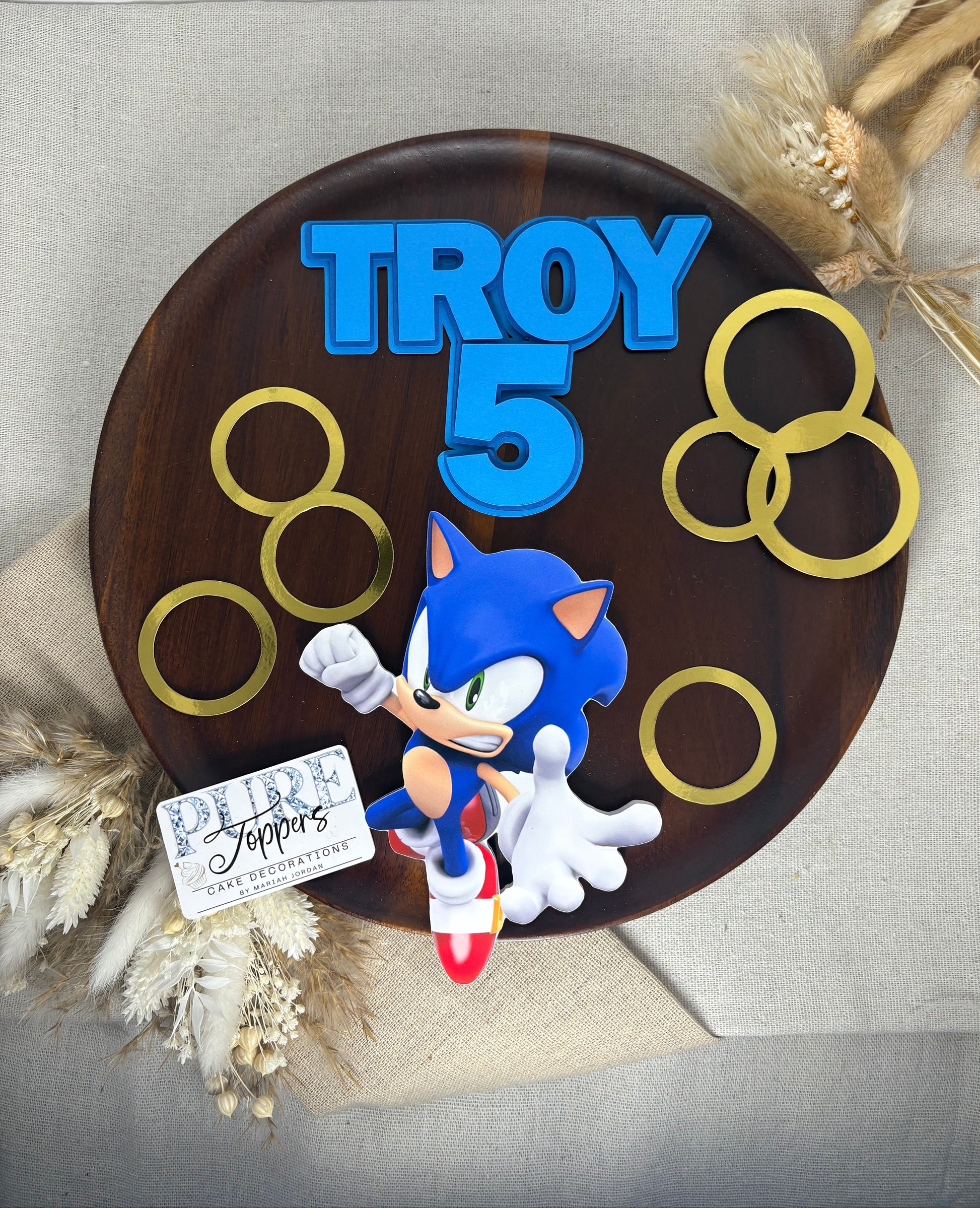Personalized birthday cake topper with Sonic the Hedgehog design and 'Troy 5' text, on a neutral background.