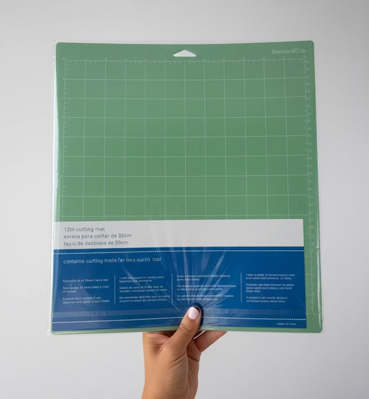 A person's hand holds a packaged green StandardGrip quilting mat with a blue and white paper label, positioned in front of a white paneled door.