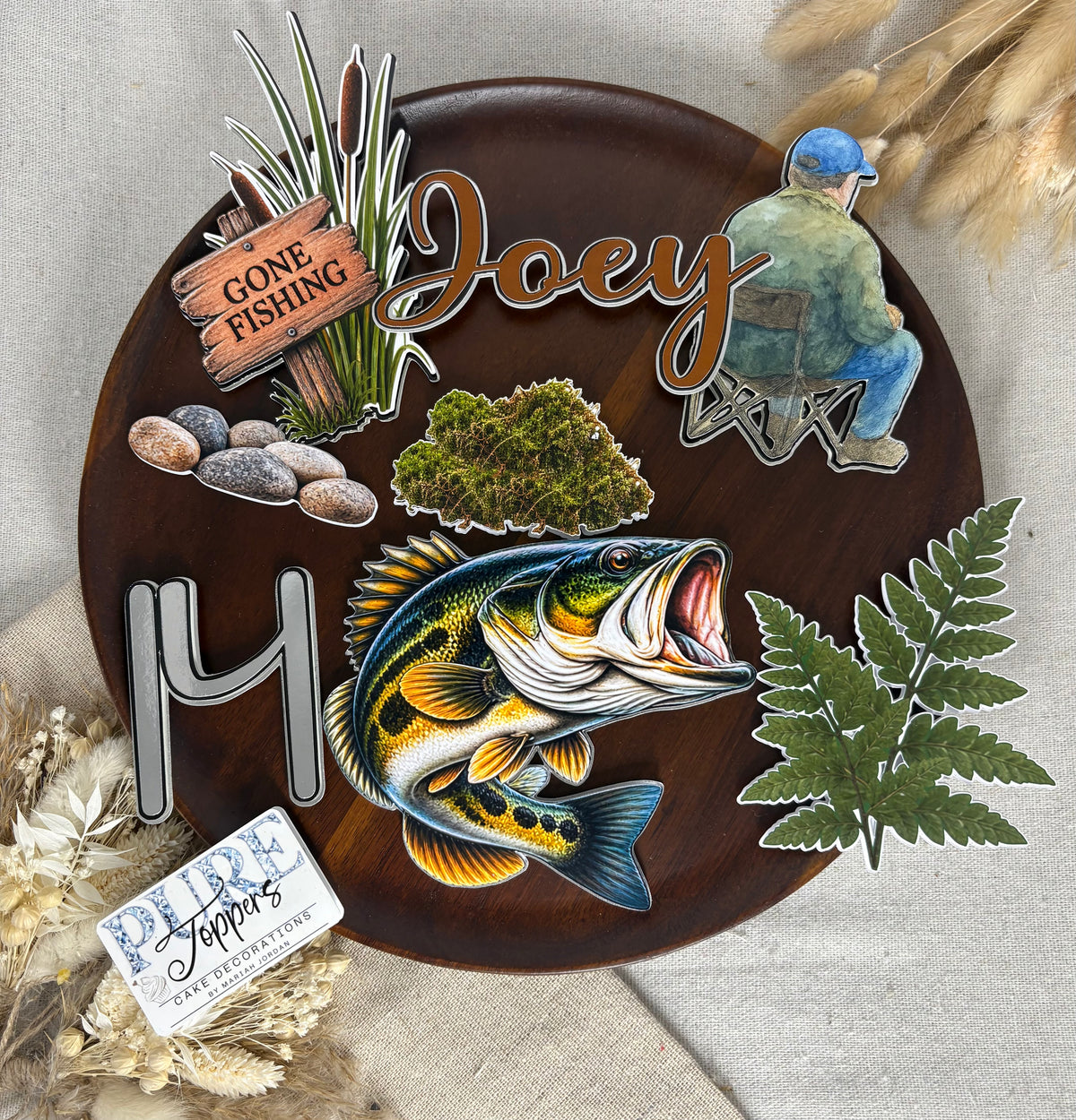 Fishing cake topper accessories featuring reeds, rocks and greenery for a nature-themed birthday cake