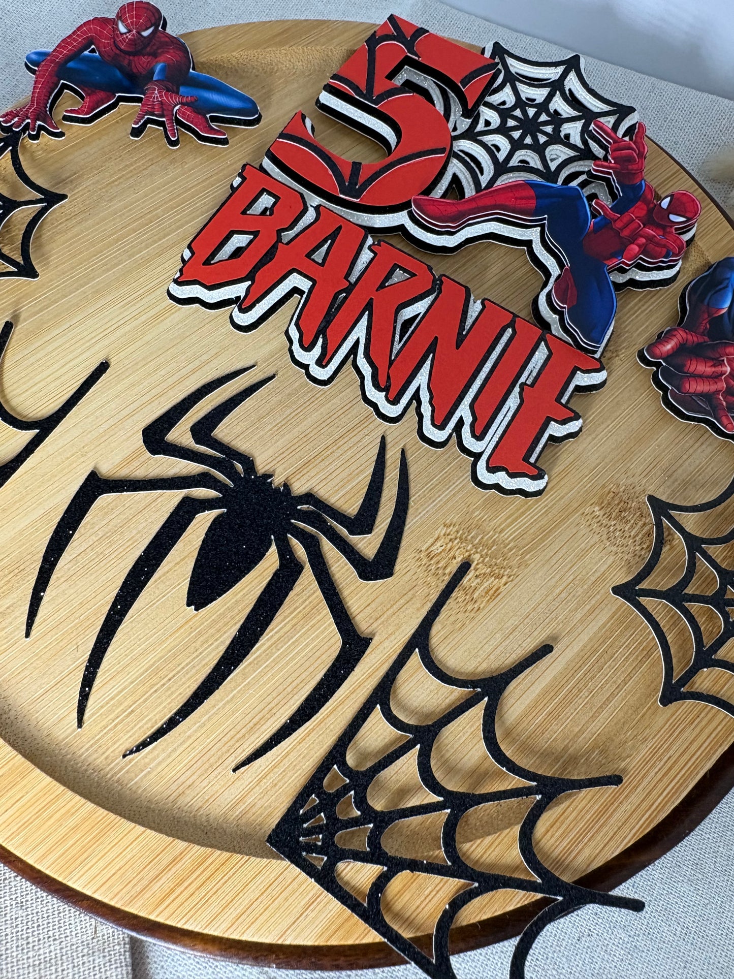 Layered Spider-Man inspired cake decorations with character, spider and web charms